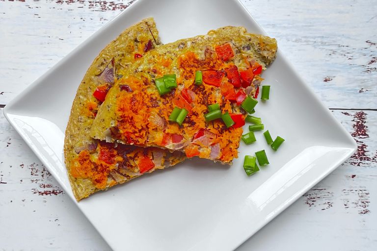 Two triangles of vegetable omelette, made with oats, on a white, square plate topped with spring onions