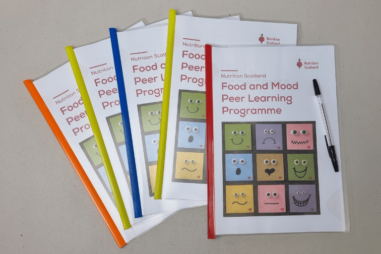 Nutrition Scotland printed text books that have red title that reads Food and Mood Peer Ambassador learning Programme. Under the title there is a grid with different faces: smiling, sad, surprised and more