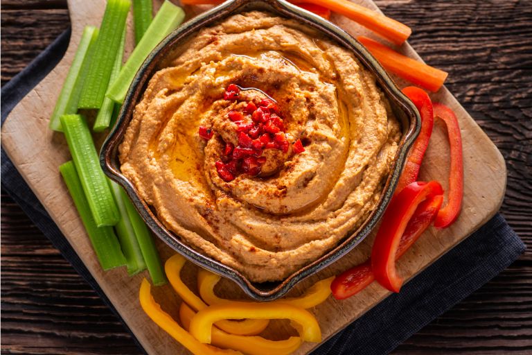 Healthy roasted red pepper hummus dip with celery and bell pepper sticks