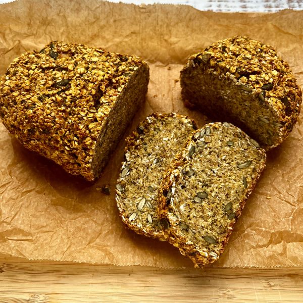 A seeded loaf of oat bread with two slices cut, placed on a piece of brown parchment paper