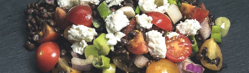 Lentil and tomato salad with cherry tomatoes, black lentils, crumbled feta cheese, and red onion on a dark slate
